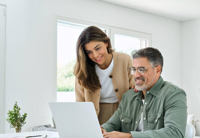 Smiling couple sitting at a desk using a laptop to research buying a home in the United States as non-U.S. citizens