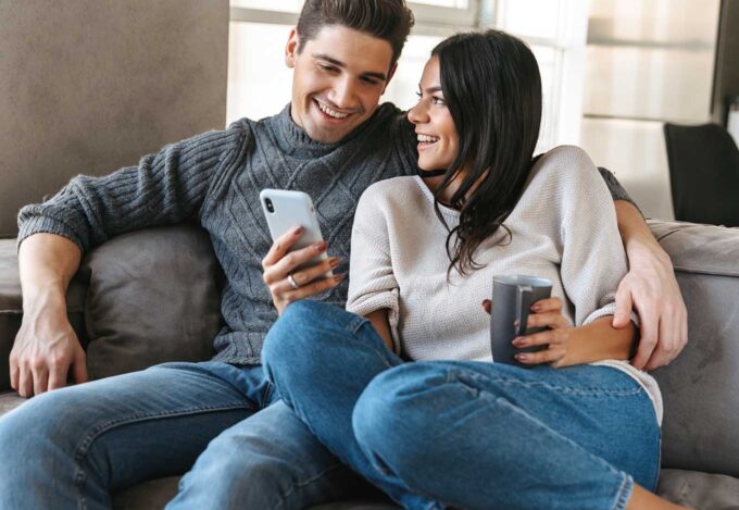 Couple sitting together on a couch researches a cash-out refinance on their cell phone.