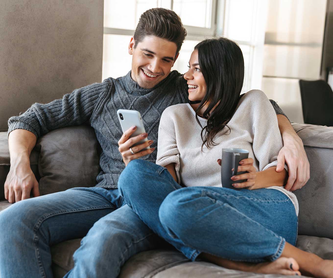 Couple sitting together on a couch researches a cash-out refinance on their cell phone.