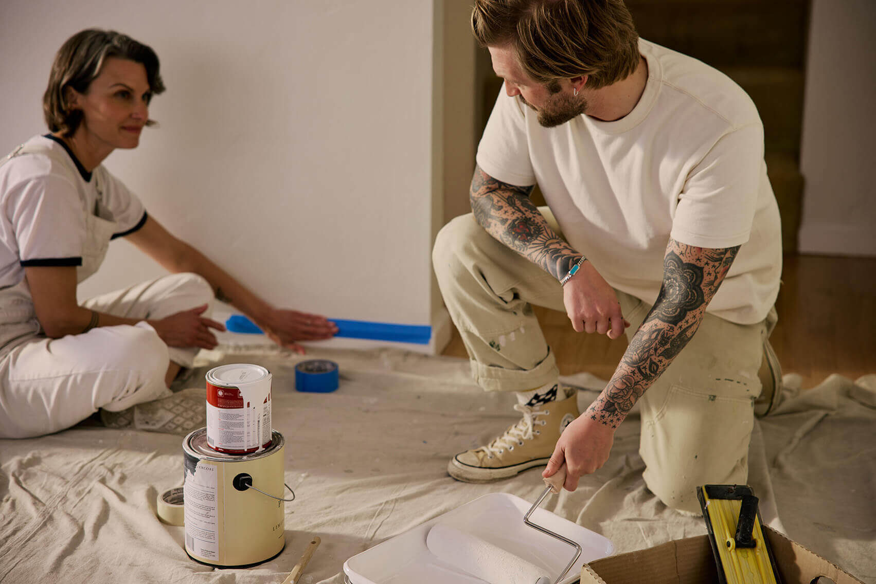 Man and woman preparing a room for painting with tape, paint cans, and tools as part of a DIY home project on a budget.