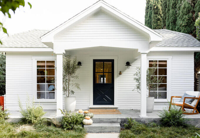 A white cottage with black front door and fall decor, a home secured with earnest money during the homebuying process.