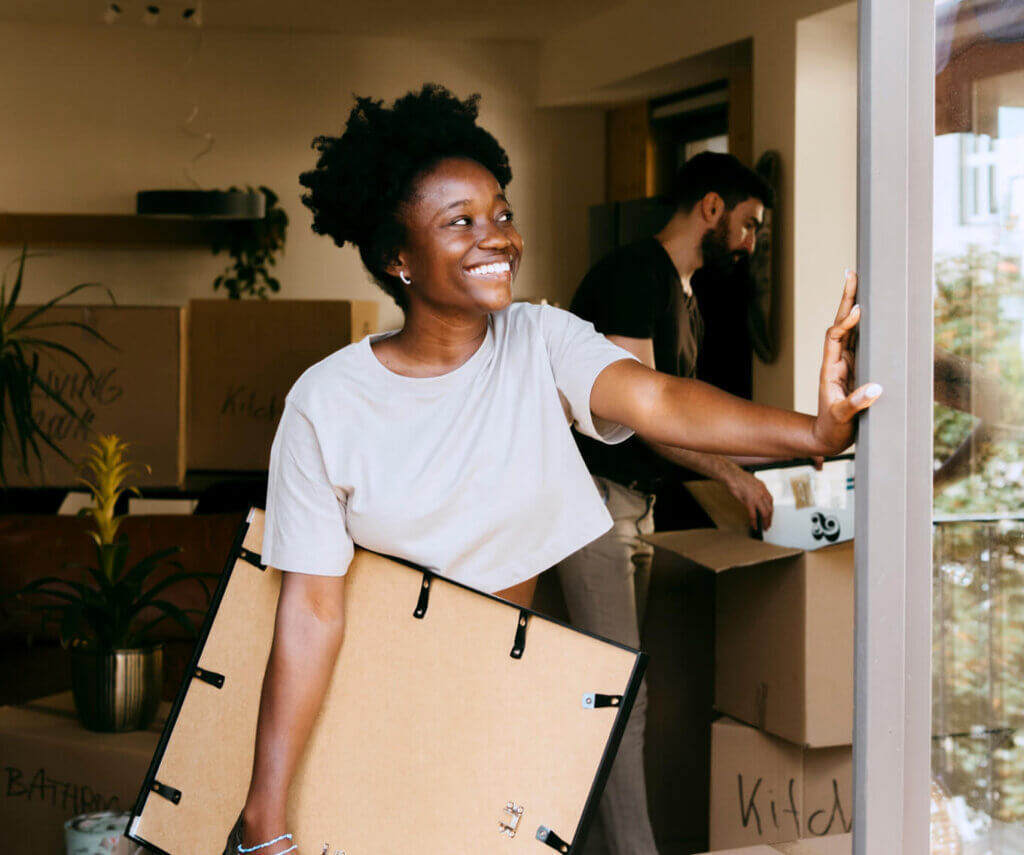 First-Time Homebuyer smiling while carrying a picture frame as they move into a home purchased using a grant.