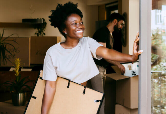 First-Time Homebuyer smiling while carrying a picture frame as they move into a home purchased using a grant.