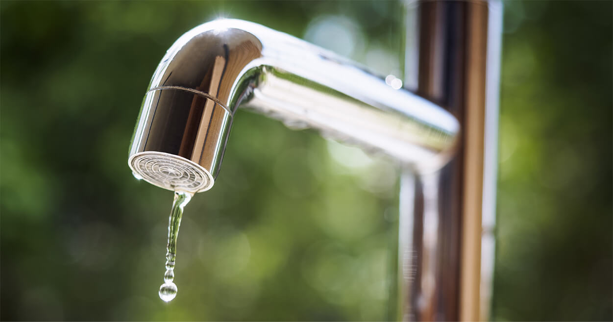 Close-up of a metal faucet with a water droplet hanging from the spout, symbolizing monthly utility expenses.