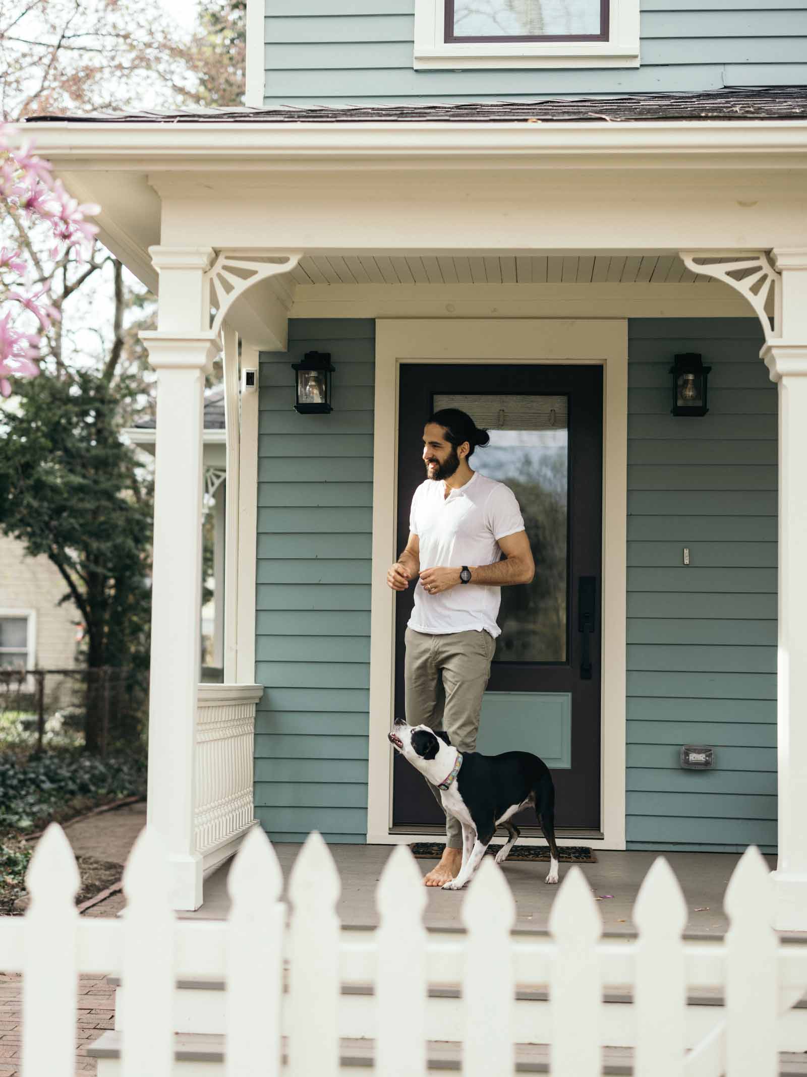 A man and his dog on the front porch of their blue house celebrate homeownership.