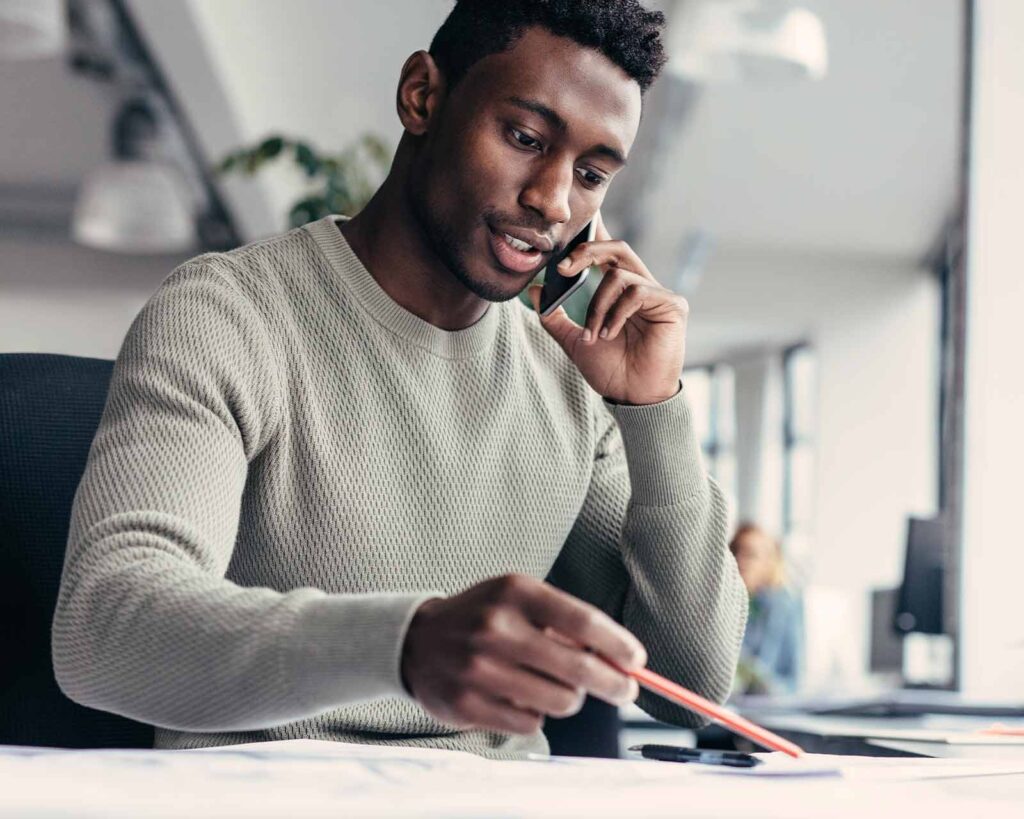 Man at desk on cell phone views refinance mortgage rates today. 