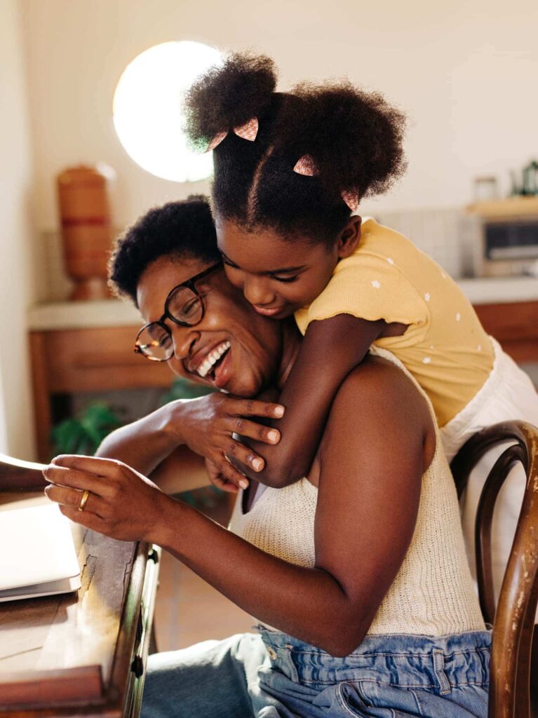 Daughter hugs mother while researching on a laptop how much home they can afford.
