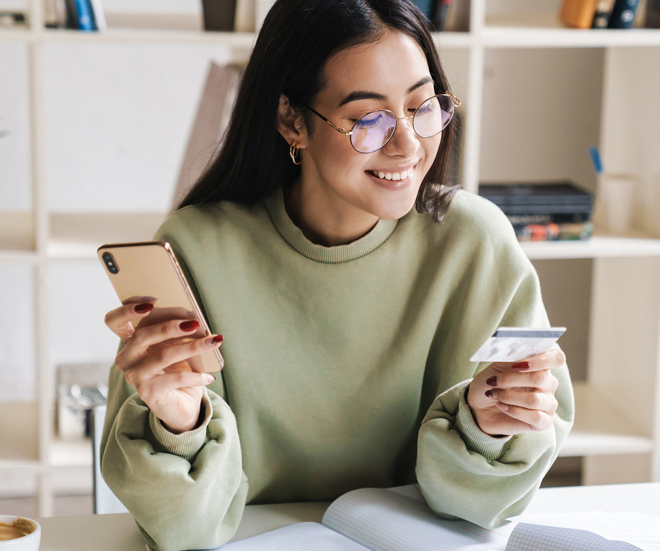 Young woman sits at desk while researching how to pay off credit card debt on her mobile phone.