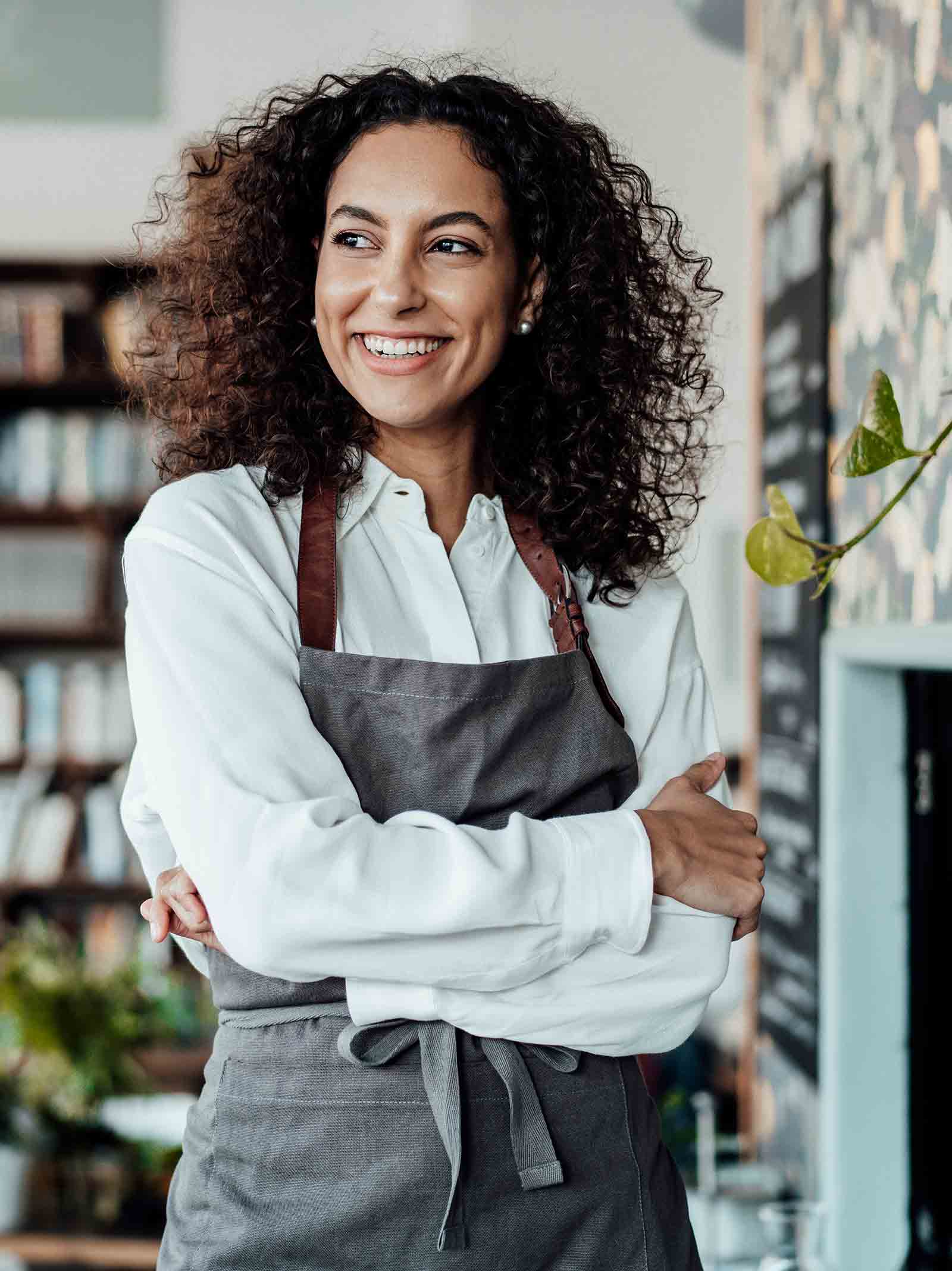 Self-employed chef wearing apron poses inside restaurant. 