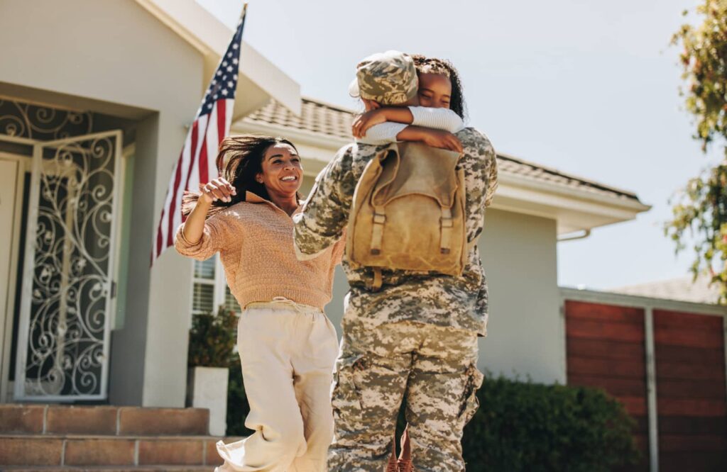 Veteran hugs child outside of a home purchased using a VA loan.