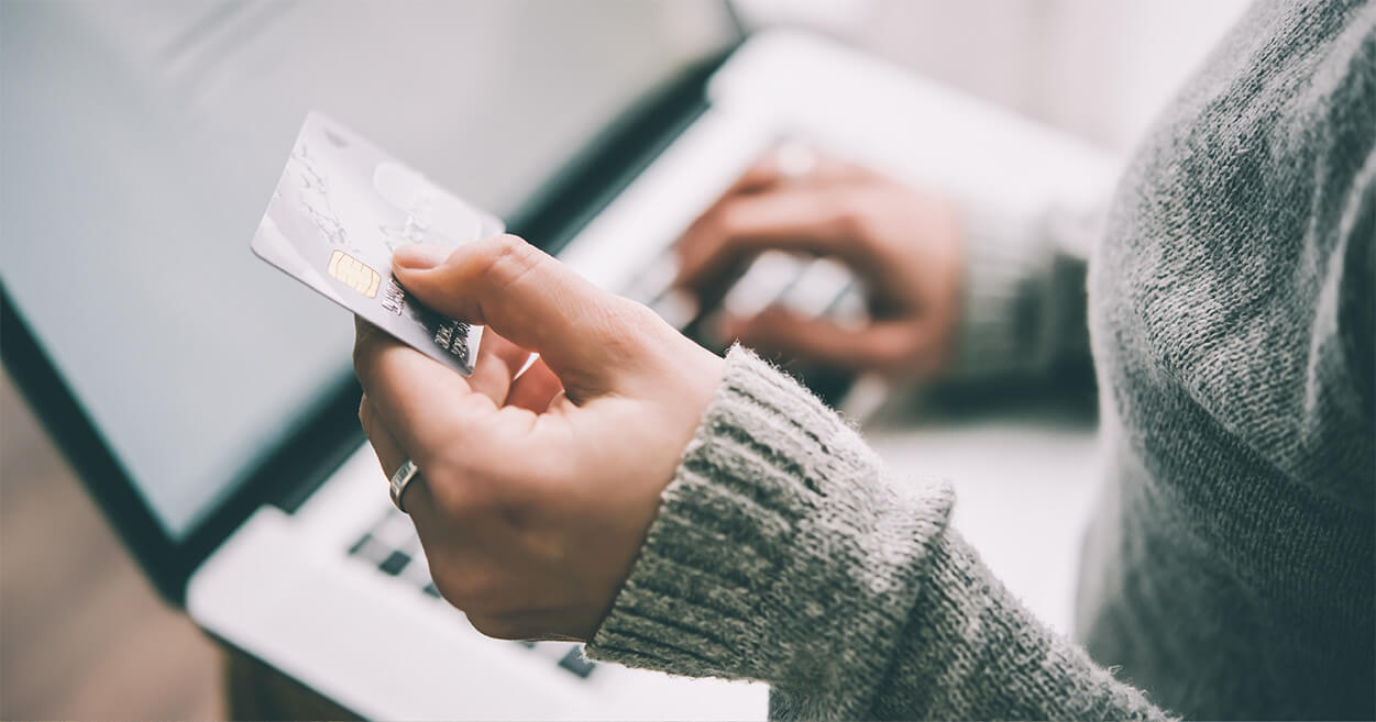 Close-up of a person in a gray sweater holding a credit card and typing credit score details on a laptop.