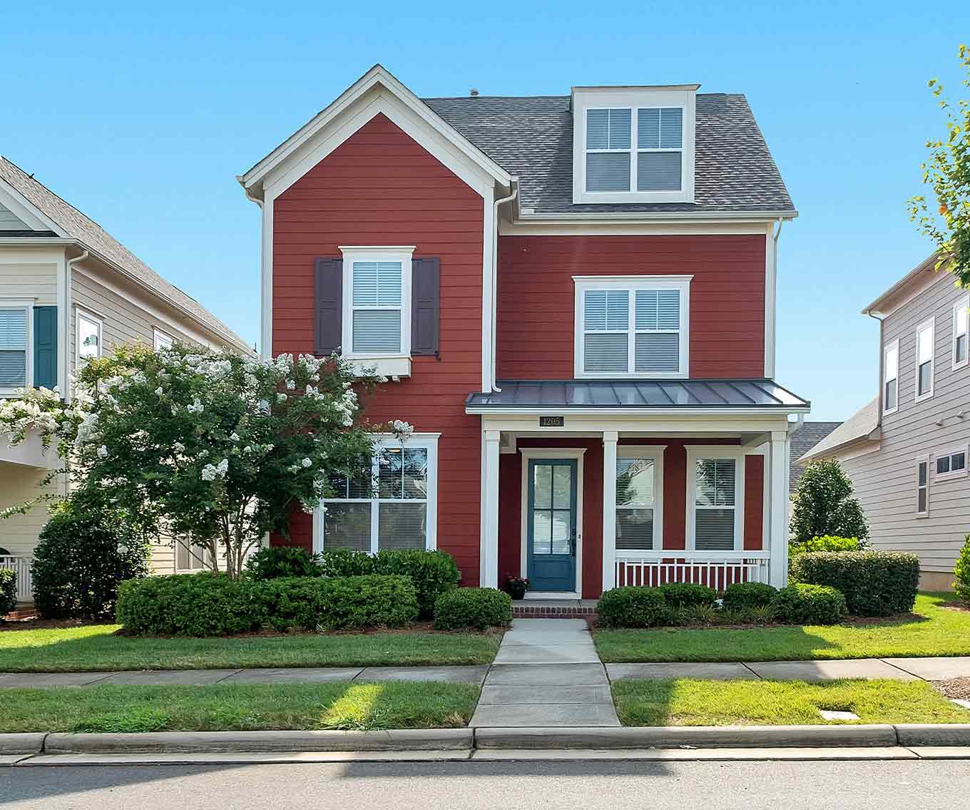 The exterior of a red 2-story home in a neighborhood from the street.